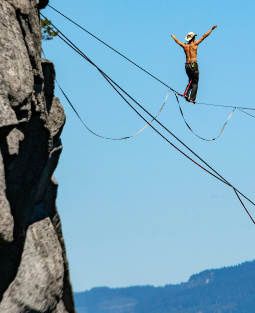 Photographie d'un homme marchant sur un fil suspendu entre deux montagnes