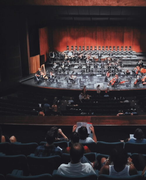 Photographie d'un théâtre avec du public et un orchestre en répétition
